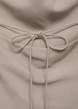 Top color beige, con cuello drapeado, diseño sin mangas, espalda abierta con cierre de lazo y dobladillo asimétrico.
