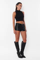 Short negro de cuerina, tiro medio, con bolsillos delanteros y traseros, presillas en la cintura y cierre con botón metálico y cremallera.