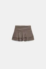 Falda pantalón de tiro medio en color negro, con diseño de pliegues en la parte superior y volantes en el ruedo. Cuenta con cierre lateral.