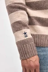 Buzo de punto con diseño de rayas horizontales en azul marino y beige, cuello redondo y puños acanalados. Presenta un pequeño bordado de estrella en la manga.