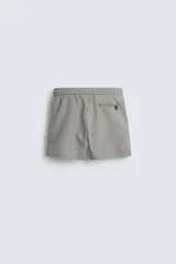 Bañador de hombre color verde claro con finas rayas blancas verticales (efecto seersucker). Tiene cintura elástica ajustable con cordón verde, bolsillos laterales y un bolsillo trasero de vivo.