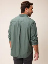 Camisa de manga larga en color azul, confeccionada en algodón con técnica de teñido garment dye. Presenta cuello abotonado, cierre frontal con botones y un bolsillo en el pecho con detalle bordado.