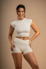 Conjunto deportivo color crema compuesto por un top corto de mangas cortas y unos shorts de tiro alto.