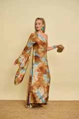 Vestido túnica largo de satén con diseño de un solo hombro, una manga larga amplia y estampa tipo tie-dye en tonos marrón y celeste.