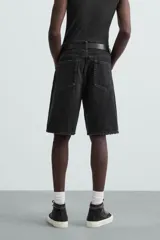 Bermuda de denim de algodón, color verde claro lavado, de corte recto y tiro medio. Presenta cinco bolsillos y cierre frontal con cremallera y botón.