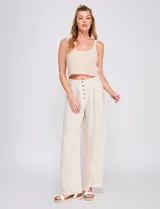 Pantalón palazzo color blanco, confeccionado en mezcla de lino y viscosa, de tiro alto con cierre frontal de botones, pinzas en la cintura y piernas anchas.