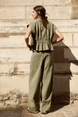 Chaleco de cuello alto y manga sisa, color verde militar, con elásticos fruncidos en la cintura y cierre frontal de botones metálicos a presión.