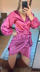 Vestido corto color fucsia de satén, con escote cruzado, mangas largas abullonadas y falda cruzada con lazo en la cintura.