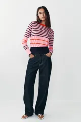 Jersey de punto de cuello redondo y manga larga con puños ajustados. Presenta un diseño de rayas horizontales en tonos rosa, azul marino y detalles en rojo.