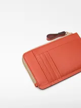 Monedero Adolfo Dominguez color ladrillo de cuero vacuno con cierre de cremallera, un compartimento y tarjetero en la parte trasera.