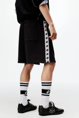 Short de felpa de mezcla de algodón en color negro, con corte regular fit, cintura elástica con cordón de ajuste y bolsillos laterales. Presenta franjas laterales blancas con el logotipo de la marca repetido y el logo de Lotto bordado en la pierna izquierda.