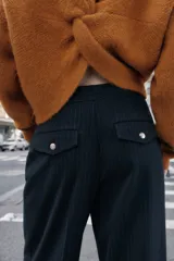 Pantalón de tiro alto color bordó, con pinzas delanteras, bolsillos frontales y falsos bolsillos con solapa en la espalda. Tiene pernera ancha y cierre frontal con cremallera, botón interior y gancho.