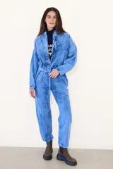 Mameluco de jean con efecto nevado estilo vintage, de corte holgado, mangas largas, cierre frontal con botones a presión y lazo ajustable en la cintura.