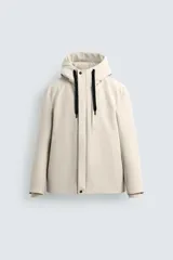 Cazadora técnica de corte regular fit, color beige, con capucha ajustable, cierre frontal de cremallera oculta por solapa con botones a presión, bolsillos laterales y puños con interior de rib.