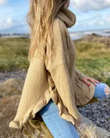 Sweater color beige de tejido de punto con cuello alto, mangas largas y corte asimétrico con volados en el ruedo.