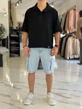 Chomba oversize blanca de lino con mangas cortas, cuello polo y cierre frontal parcial de dos botones. Cuenta con una pequeña etiqueta decorativa en el borde inferior.