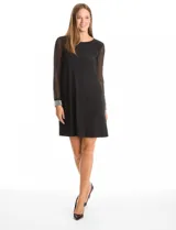 Vestido negro de seda fría con silueta evasé, cuello redondo y mangas largas de gasa transparente. Los puños son anchos y están decorados con una densa aplicación de perlas blancas.