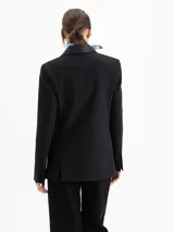 Blazer negro de corte sastrero con solapas en cuero vacuno. Presenta cierre frontal con broches forrados, bolsillos laterales con tapa y bolsillo relojero. Cuenta con tajos en la espalda y un largo que sobrepasa la cadera.