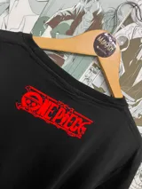 Remera negra de algodón con estampado de personajes de One Piece en colores azul, naranja y rojo.