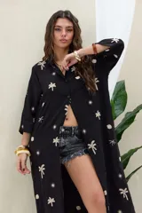 Camisola larga de color negro con bordados en tono beige de palmeras, soles y conchas. Cuenta con cuello camisero, cierre frontal con botones, mangas largas y bolsillos frontales.
