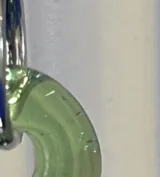 Aros tipo argolla con dije colgante en forma de dona de vidrio color verde traslúcido. La estructura de la argolla es de plata 925.