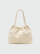 Bolso tipo tote de cuero color crema, con frunce superior y asas de hombro. Presenta un pequeño bolsillo frontal con cierre metálico dorado y un dije de llave colgante.