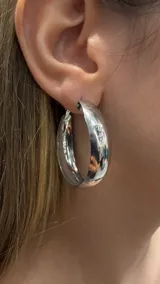 Aros tipo argolla de tamaño mediano con diseño grueso y superficie lisa brillante en color plateado.