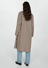 Abrigo largo de diseño oversize con tejido de lana, cuello con solapas de muesca y cierre frontal de doble botonadura. Presenta hombros caídos, manga larga y dos bolsillos laterales, con una abertura posterior en el bajo.