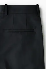 Pantalón sastrero de sarga en color negro, con corte holgado, piernas amplias con raya marcada, cierre frontal con botón y corchete ocultos, bolsillos al bies y bolsillos traseros insertados.