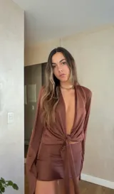 Vestido corto de satén color marrón, compuesto por una blusa de manga larga con escote profundo y nudo frontal, y una falda ajustada a juego.