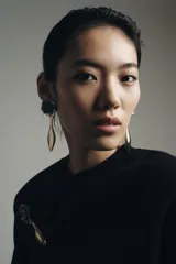 Maxi pendientes colgantes con diseño de flor en relieve en tonos blanco y negro, unidas a una pieza metálica dorada con forma de jarrón alargado.