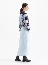 Pollera midi de denim en color azul claro con efecto lavado. Presenta un diseño de corte recto con costuras decorativas visibles, bolsillos frontales tipo cargo y una abertura central en el ruedo.