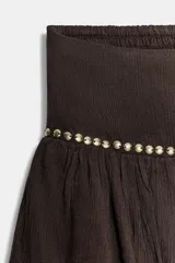 Falda pantalón corta de tiro medio, color negro, con cintura elástica en la espalda. Presenta detalle de tachas metálicas en la parte delantera y diseño de volantes a tono. Incluye forro interior.