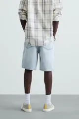 Bermuda de denim de algodón, color verde claro lavado, de corte recto y tiro medio. Presenta cinco bolsillos y cierre frontal con cremallera y botón.