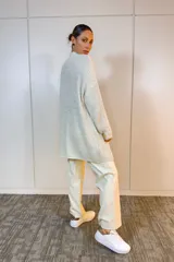 Sacón de punto largo en color beige, con diseño oversize, cuello redondo y mangas largas. Presenta una textura acanalada y un estilo abierto sin cierres.