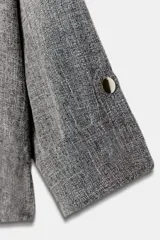 Chaqueta corta gris de tejido texturizado con cuello solapa, manga larga con trabilla, bolsillos delanteros con solapa y cierre frontal de botones metálicos.