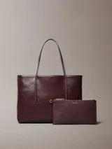 Cartera tote pequeña Calvin Klein de color bordó, con estampado geométrico de monograma, doble asa de mano y monedero o cartera mini interior a juego con cierre y logo dorado.