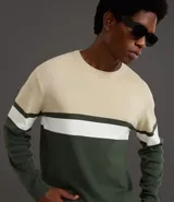 Suéter de punto con cuello redondo y manga larga, diseñado con un patrón de bloques de color en tonos beige, blanco y gris. Presenta un corte regular que se ajusta de forma anatómica al cuerpo.