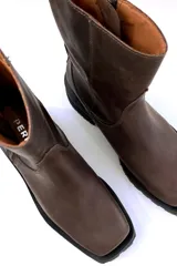 Bota de cuero color chocolate, con caña media, cierre lateral y tachas decorativas en la parte trasera.