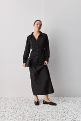 Camisa blanca de manga larga con textura suave y caída liviana, cuello camisero, puños anchos y fruncidos sutiles en los hombros.