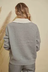 Saco de punto gris con detalles en color crema en el cuello, puños y bolsillo frontal. Presenta cierre frontal con botones y diseño de manga larga.