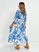 Vestido camisero midi de algodón con estampado floral en tonos rosados y blancos. Tiene cuello camisero, mangas 3/4, botones frontales, falda escalonada y cinturón fino.