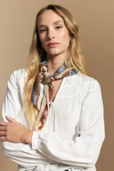 Camisa de manga larga color blanco, con cuello mao y escote en V. Presenta frunces en el canesú, cierre frontal con botones y mangas amplias con puños abotonados.