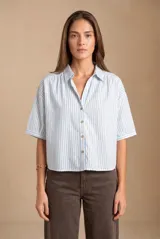 Blusa de manga corta con diseño a rayas verticales celestes y blancas, cuello camisero con escote en V y cierre frontal de botones.