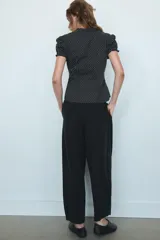 Pantalón fluido de tiro medio color verde militar, con cintura elástica en la parte trasera, pinzas en el delantero y bolsillos laterales ocultos en la costura. Presenta un diseño de pernera ancha y corte tobillero, con cierre frontal de cremallera y botón.