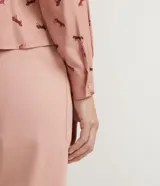 Camisa de viscosa color rosa con estampado de caballos en marrón. Tiene cuello camisero, cierre con botones, mangas largas, un bolsillo frontal y detalle de vivo contrastante en el bolsillo.