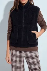 Chaleco negro de corderito sintético con cuello alto, cierre frontal y bolsillos delanteros amplios con ribetes.