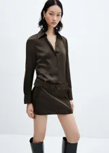 Vestido corto de satén color marrón oscuro, con cuello camisero, cierre frontal de botones y mangas largas con puños abotonados. Incluye un cinturón desmontable con hebilla a tono y cierre lateral con cremallera invisible.