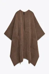 Capa de punto color marrón, con escote en V, mangas cortas y bolsillos de plastrón en el delantero. El ruedo tiene un corte asimétrico.