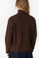 Campera de punto tejido color beige con diseño de ochos, cuello alto y cierre frontal completo.